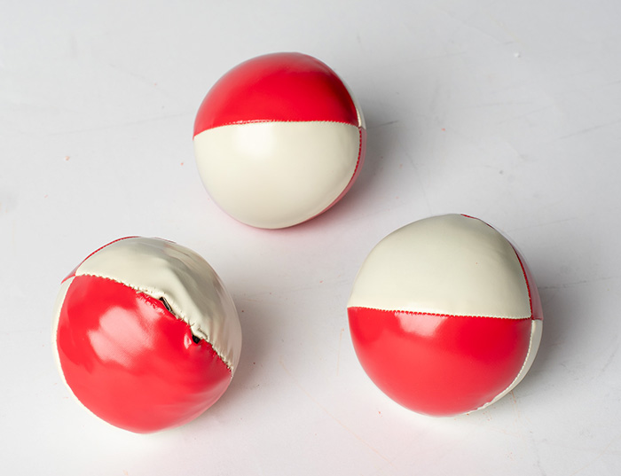 The three finished MUJU juggling balls in red and white on a studio background, one showing the stitched opening for the hidden electronics