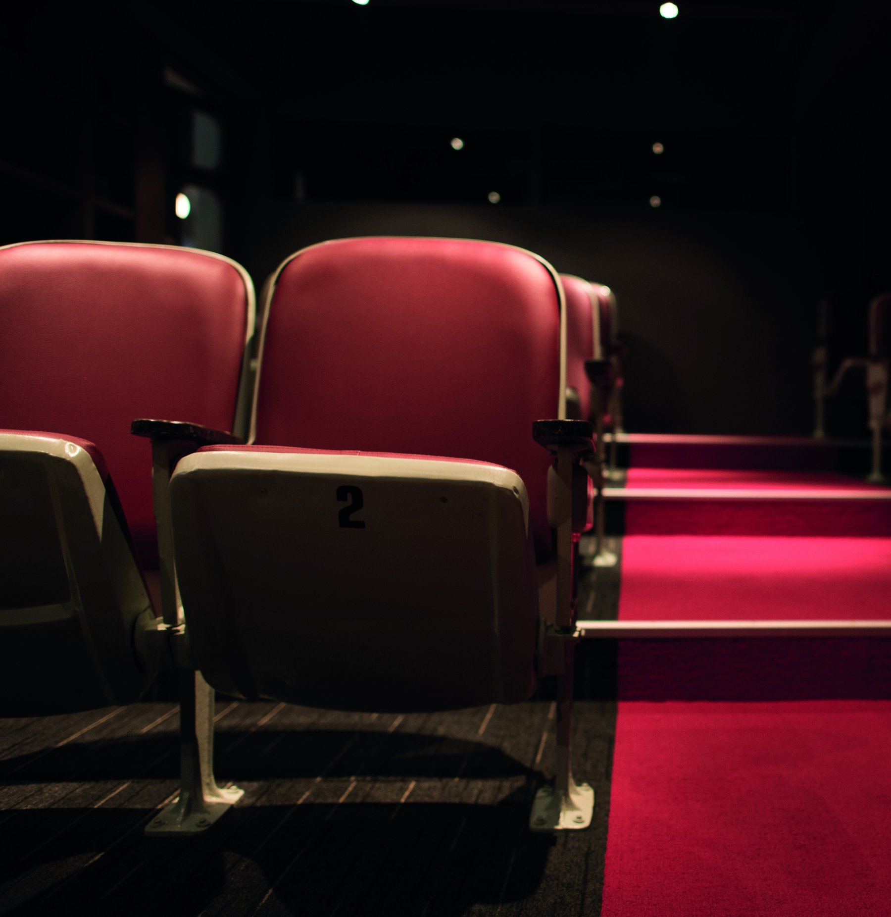 Close-up of empty red velvet cinema seats in a dark auditorium, numbered seat two in front