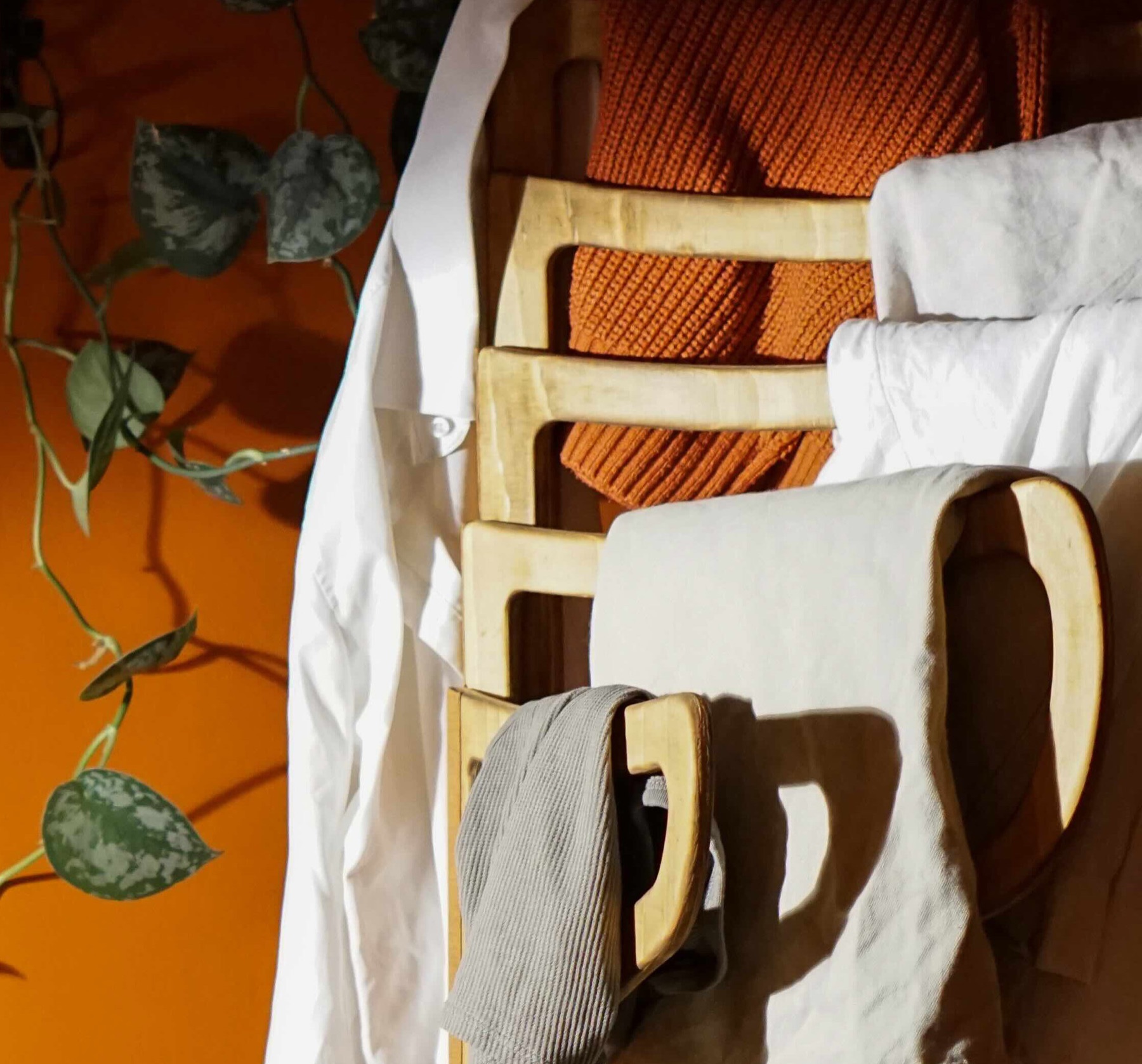 Detail of linen shirts and a knit sweater draped over Relief's wooden frame against an orange wall
