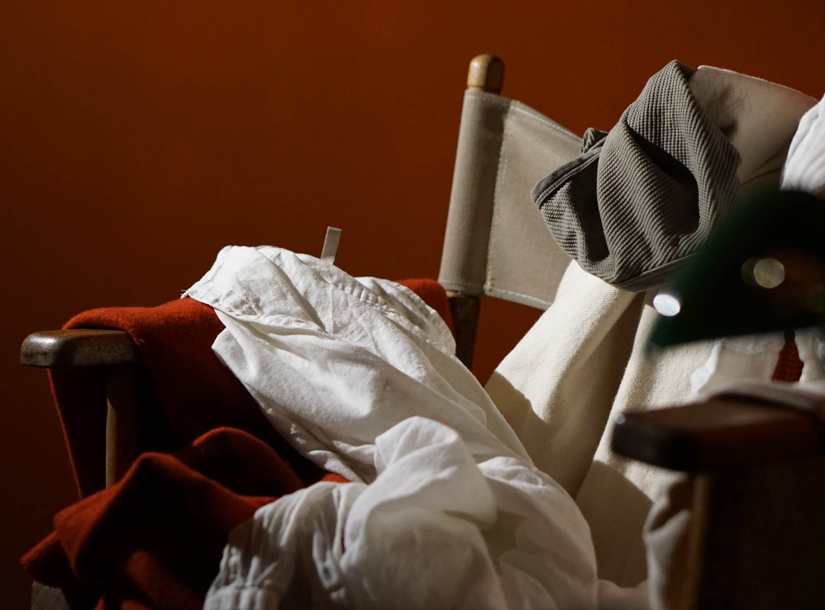 Close-up of shirts and a knit sweater piled over a director's chair in warm evening light